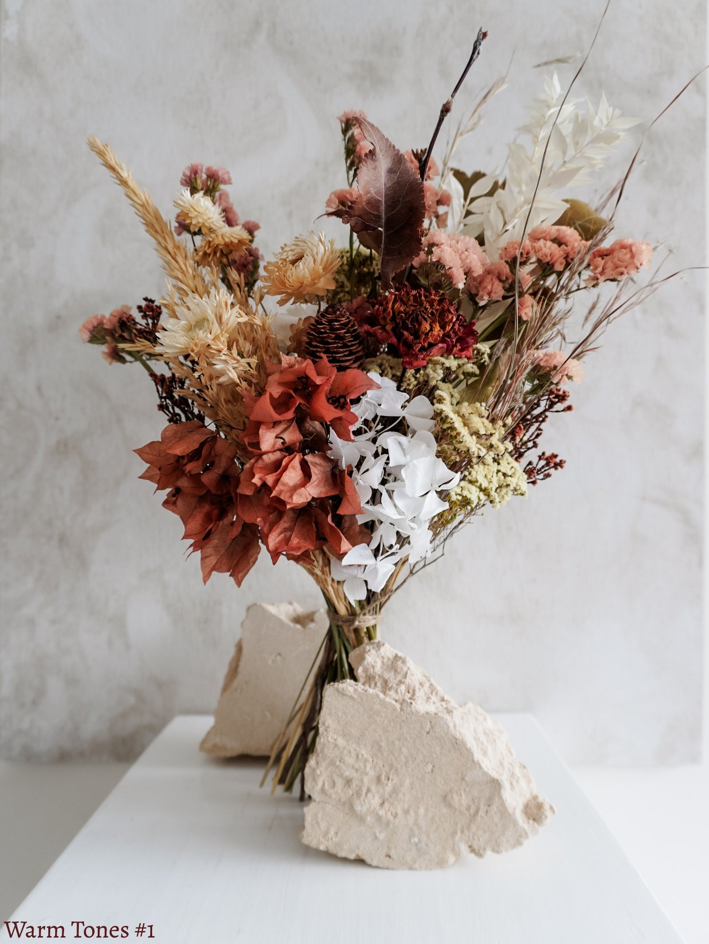 A dried flower bouquet featuring autumnal tone flowers against a textured light gray background.