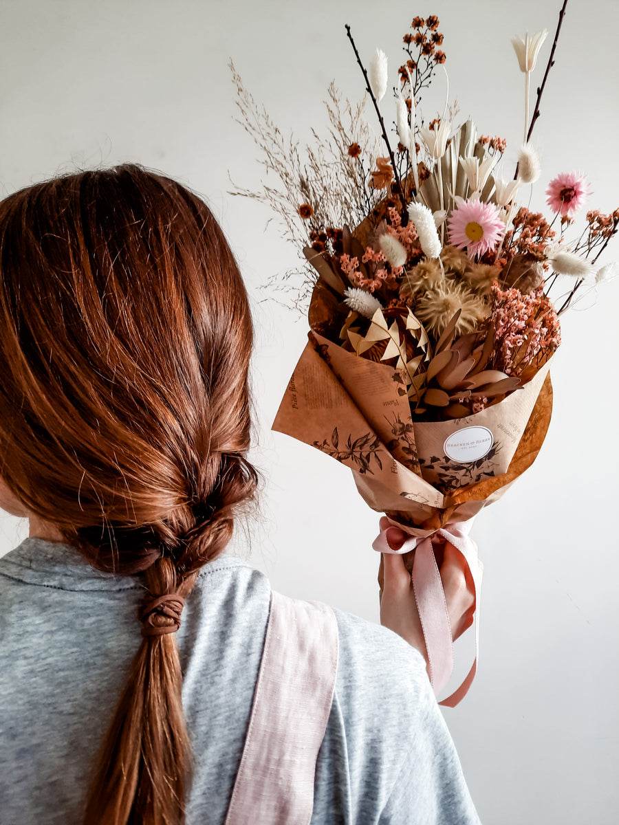 Florist holding a dried flower bouquet in pink & coral tones; handmade in Perth, Western Australia.