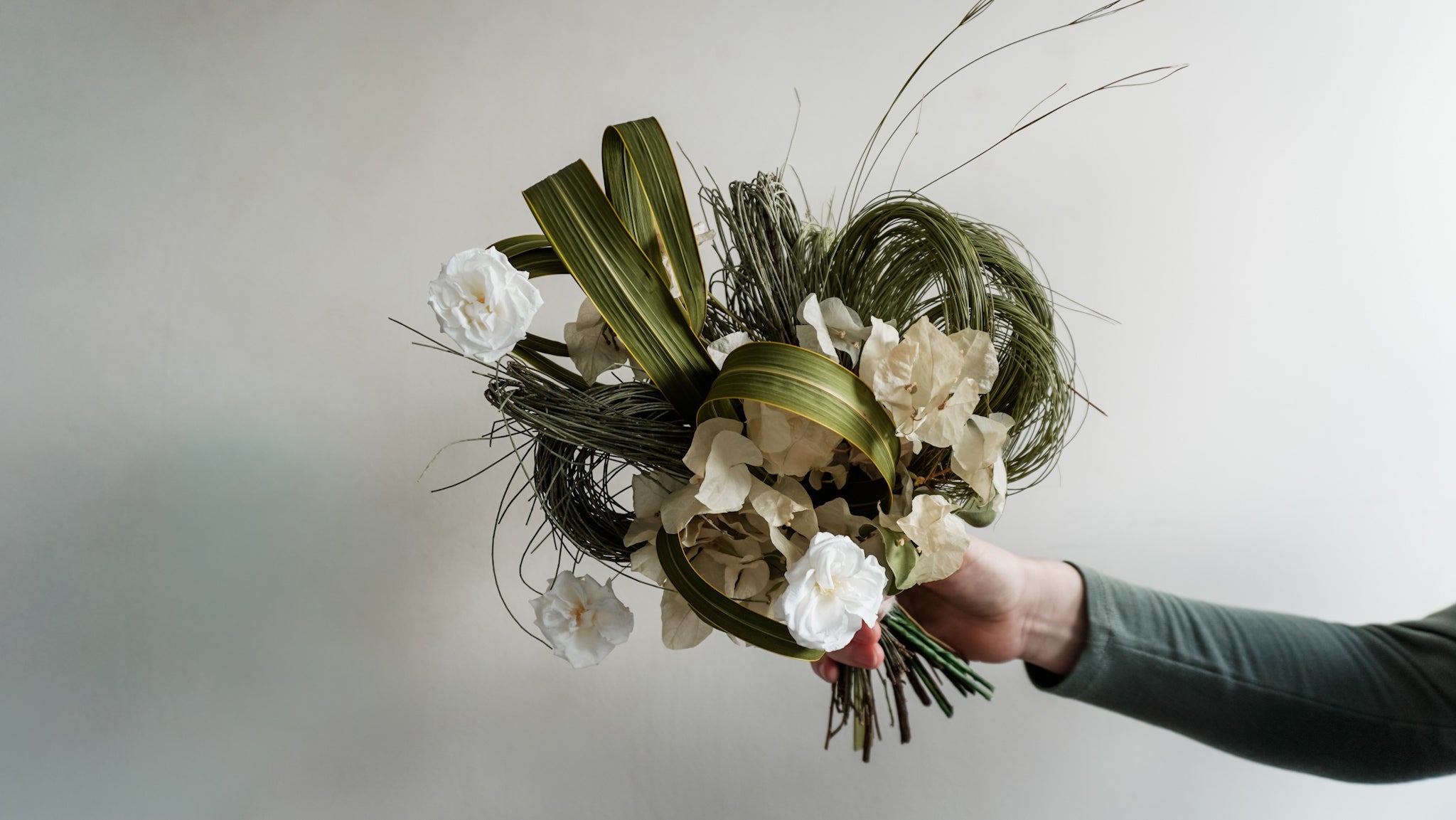Bridal bouquet of dried flowers held against a plain background.