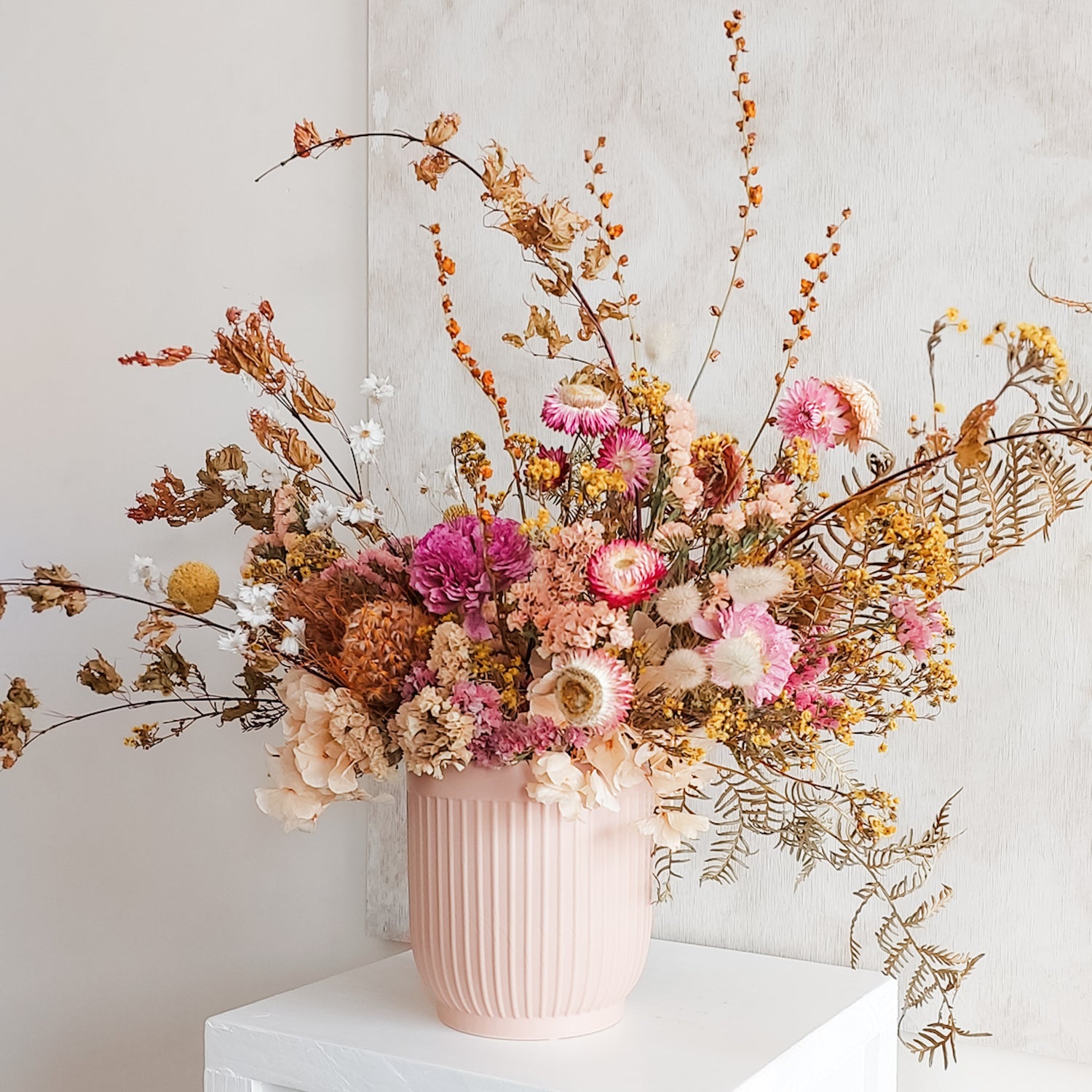Dried flower arrangement in a bright colourful palette in a nude ceramic vase.