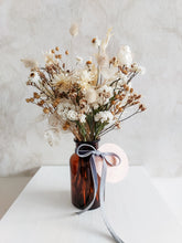 Load image into Gallery viewer, Dried flower arrangement in amber bottle vase with neutral white florals – close full view.
