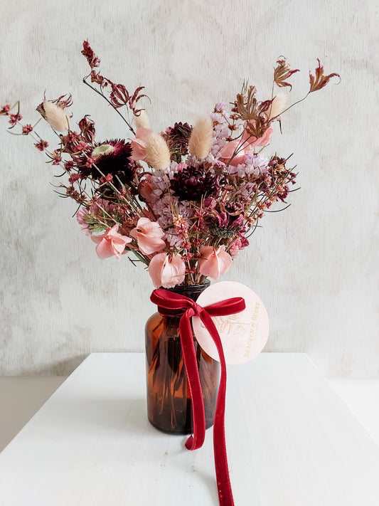 Dried flower arrangement in amber bottle vase with pink florals – close full view.
