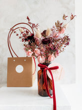 Load image into Gallery viewer, Dried flower arrangement in amber bottle vase with pink florals – vase and gift bag.
