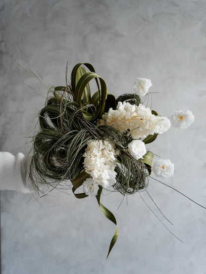 Bridal bouquet of white preserved roses and greenery held against a gray background.