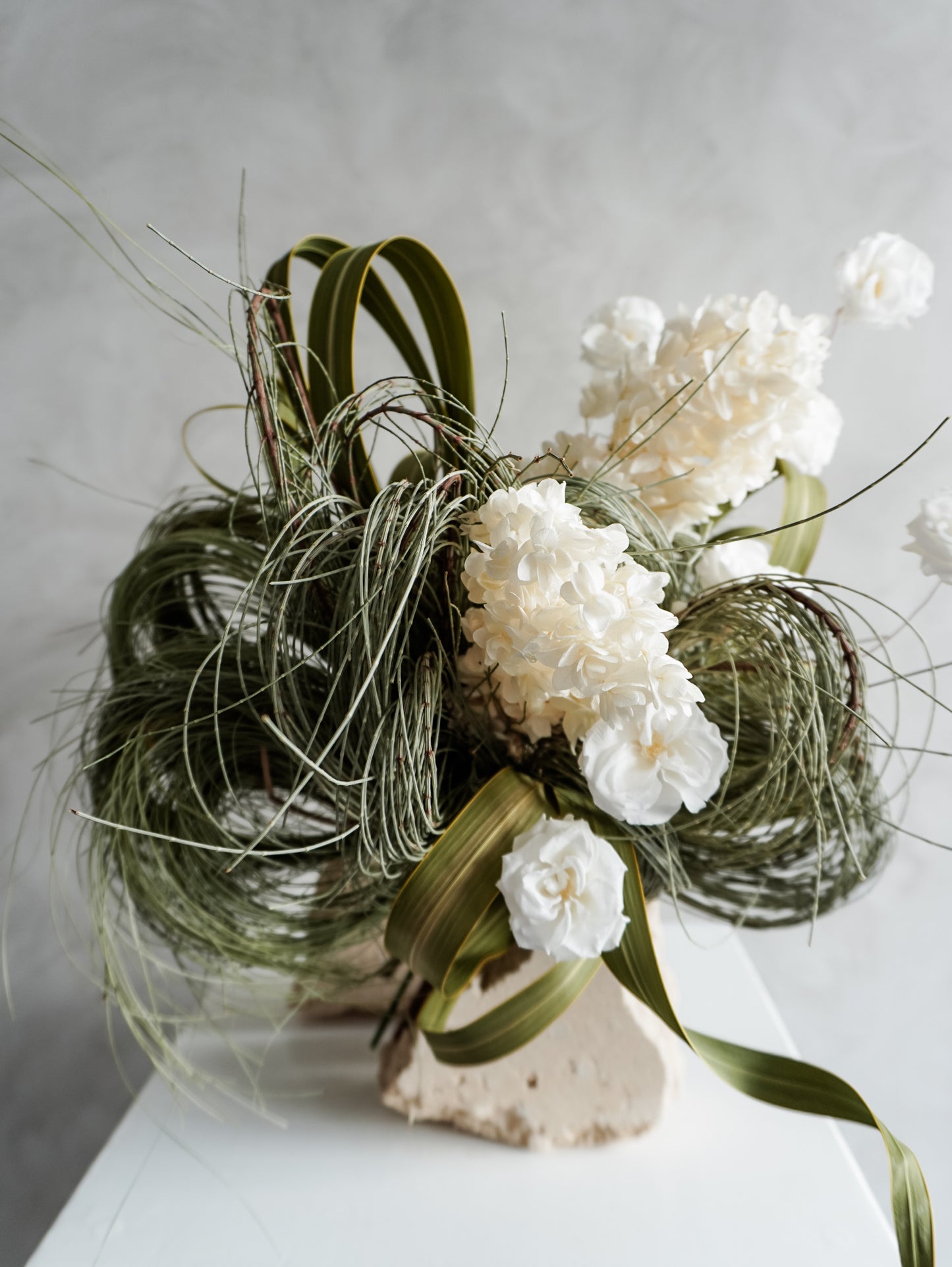 Bridal bouquet of dried white flowers and greenery on a neutral background.