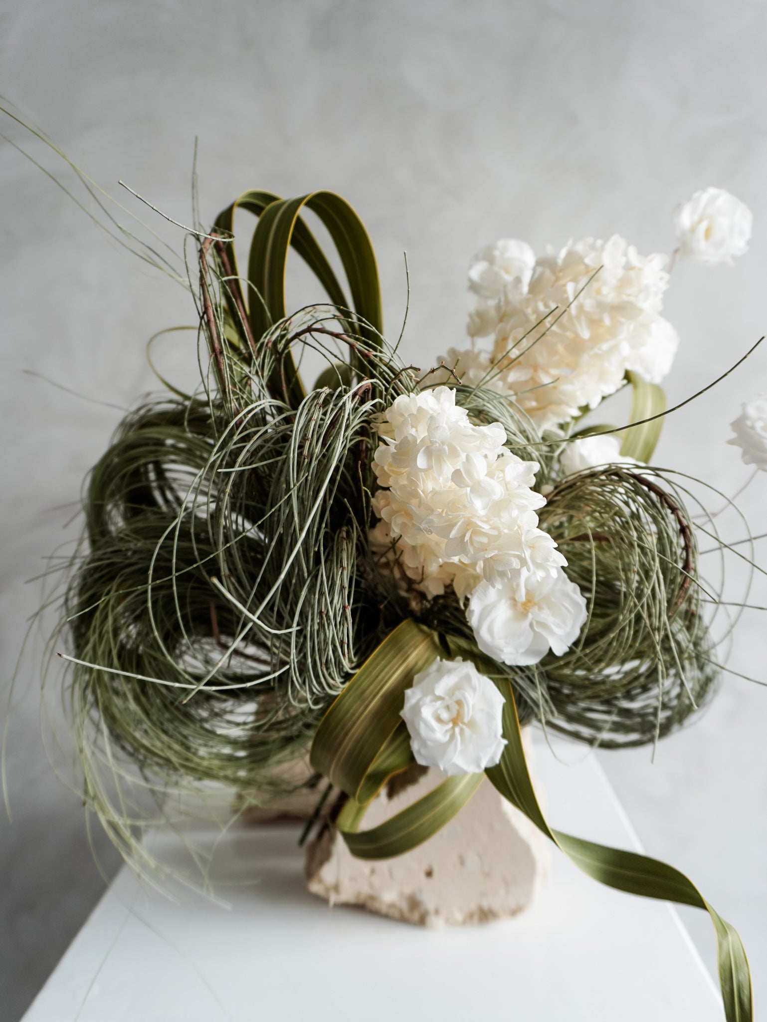 Bridal bouquet of dried white flowers and greenery on a neutral background.