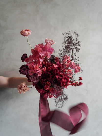 Bridal bouquet of dried and preserved pink and burgundy flowers  with ribbon on a gray background.