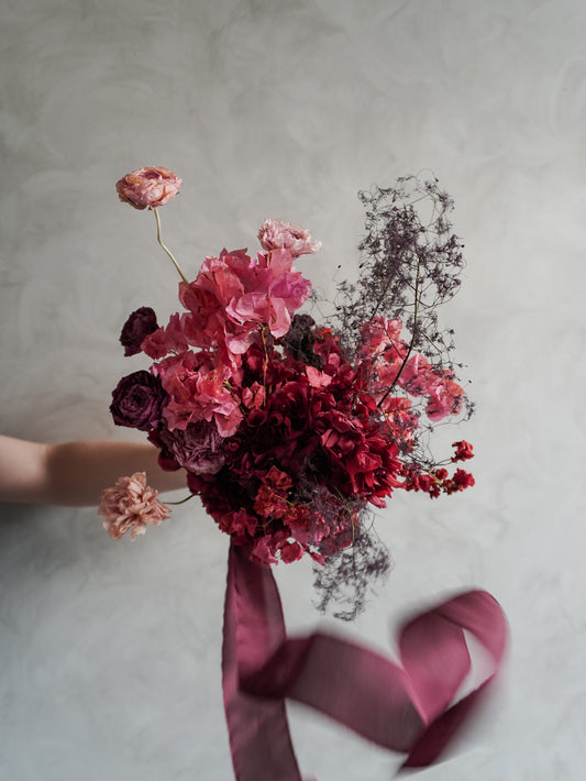 Bridal bouquet of dried and preserved pink and burgundy flowers  with ribbon on a gray background.