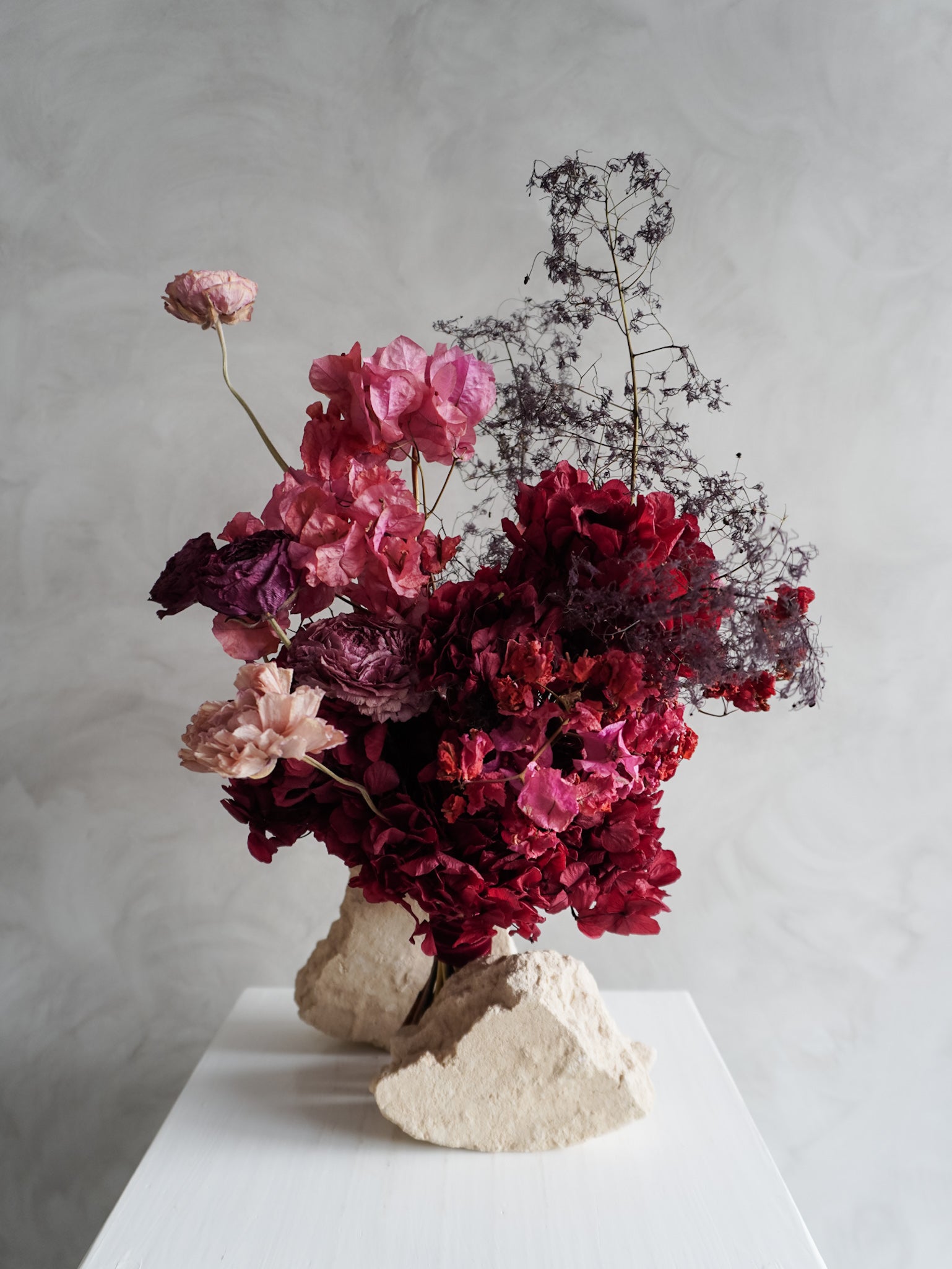 Bridal bouquet of dried and preserved pink and burgundy flowers on a gray background.