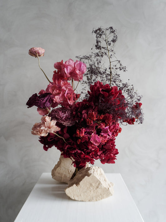 Bridal bouquet of dried and preserved pink and burgundy flowers on a gray background.