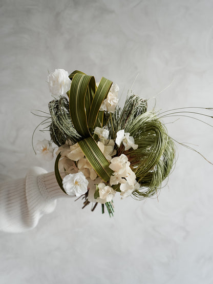 Bridesmaid bouquet of preserved white roses and greenery on a light gray background.