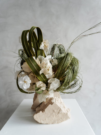 Bridesmaid bouquet of preserved white roses and greenery on a white plinth against a plain background.