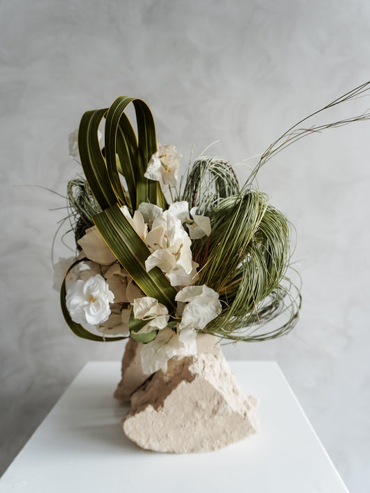 Bridesmaid bouquet of preserved white roses and greenery on a white plinth against a plain background.