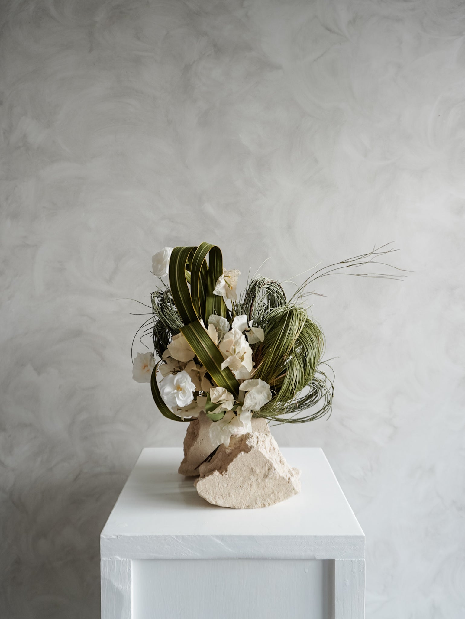 Bridesmaid bouquet of preserved white roses and greenery on a white plinth against a plain background.
