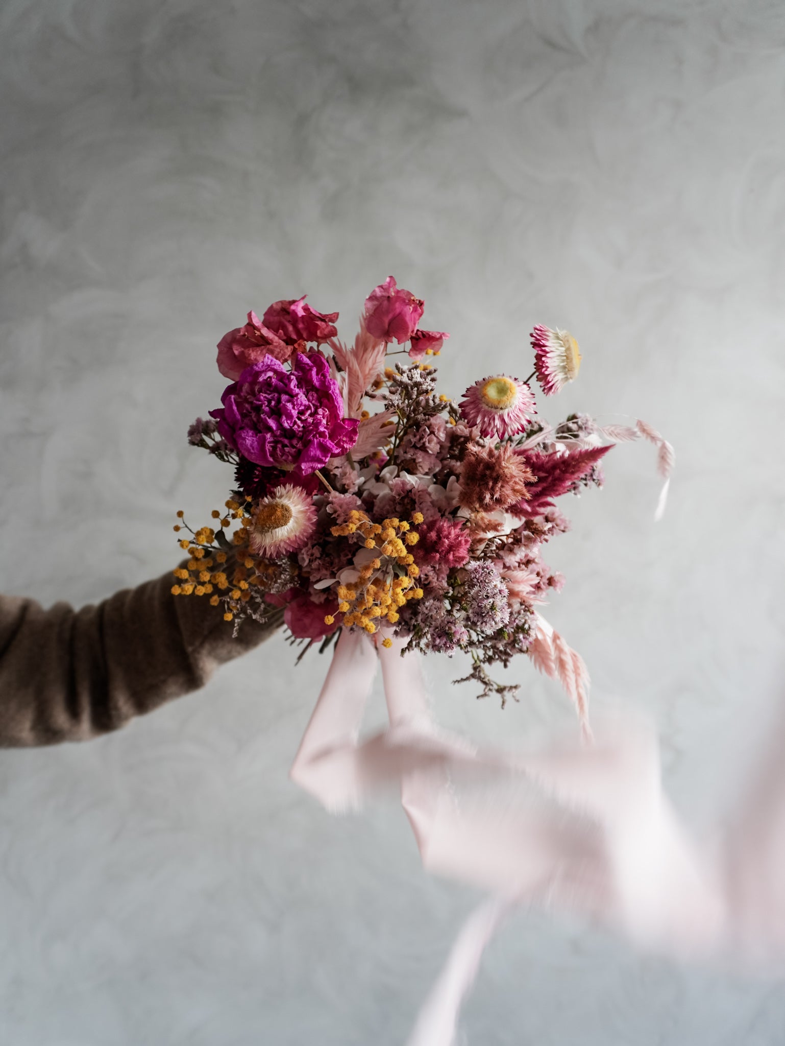 Bridesmaid bouquet of colorful dried flowers held against a neutral background.