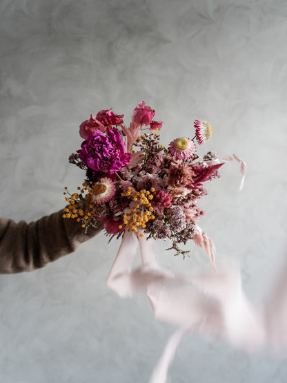 Bridesmaid bouquet of colorful dried flowers held against a neutral background.