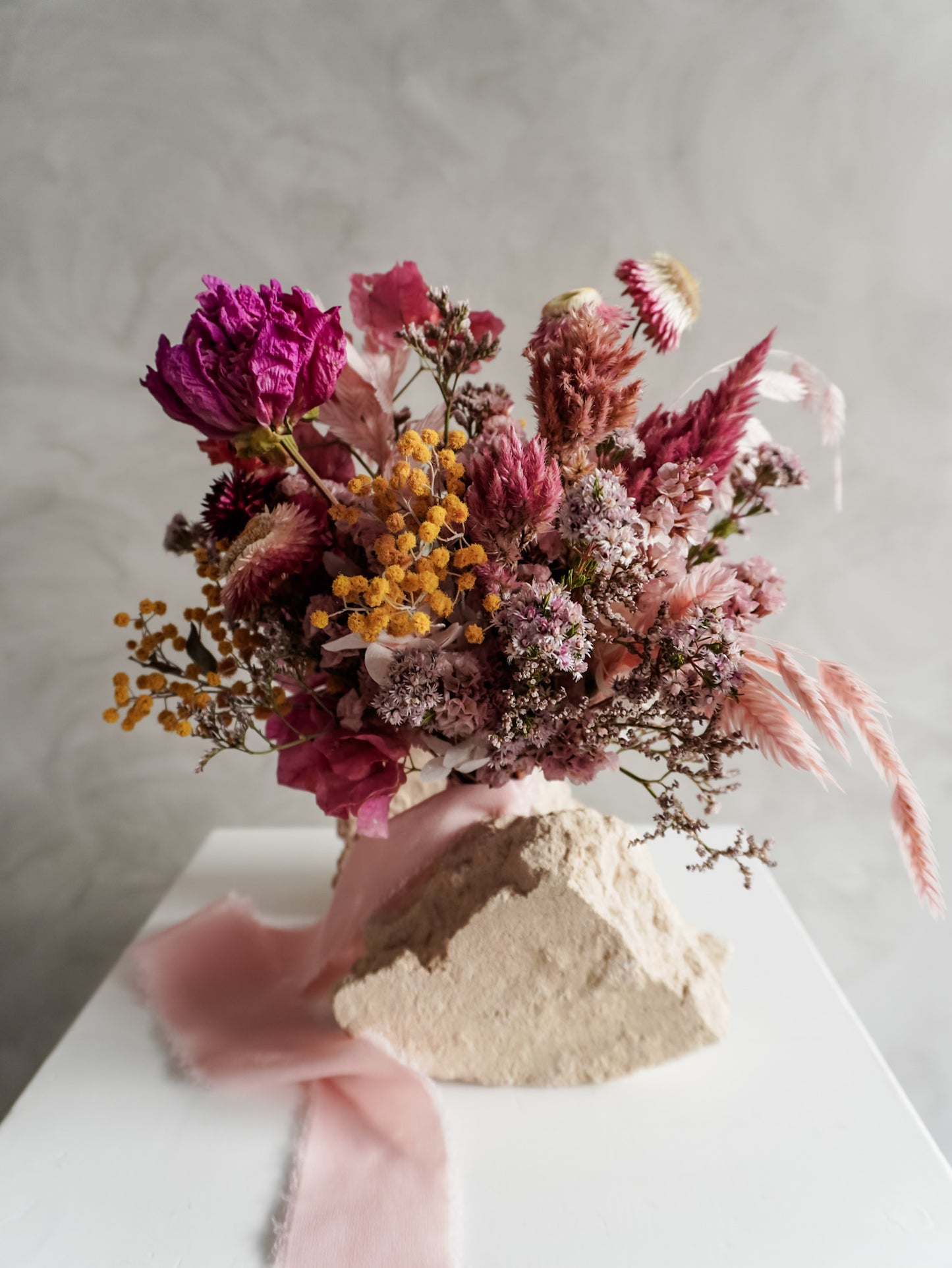 Bridesmaid bouquet of dried flowers with pink and purple tones on a neutral background.