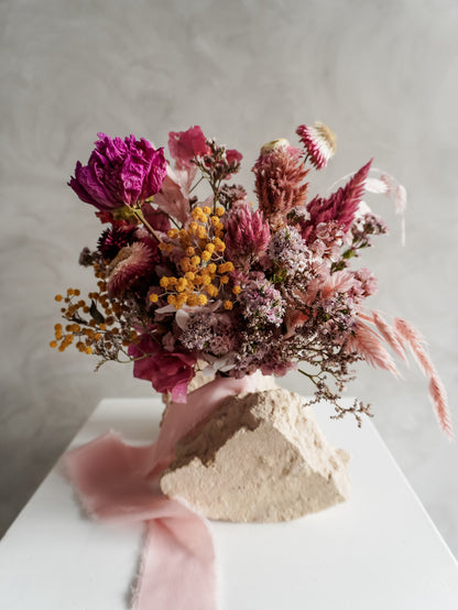 Bridesmaid bouquet of dried flowers with pink and purple tones on a neutral background.