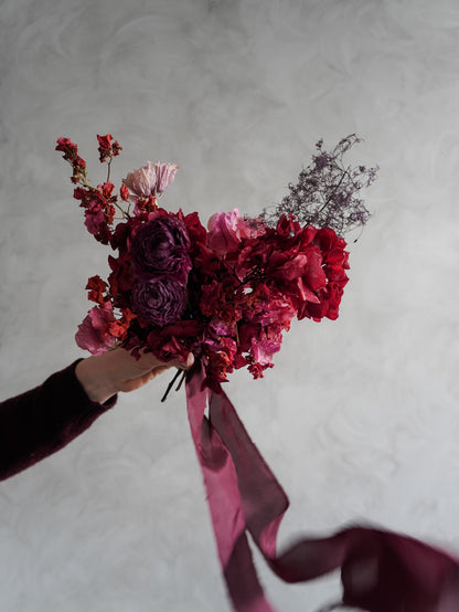 Bridesmaid bouquet of dried red and pink flowers held against a gray background.