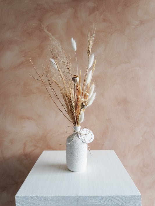 Dried flower arrangement in ceramic bud vase with white and neutral florals – distant view.