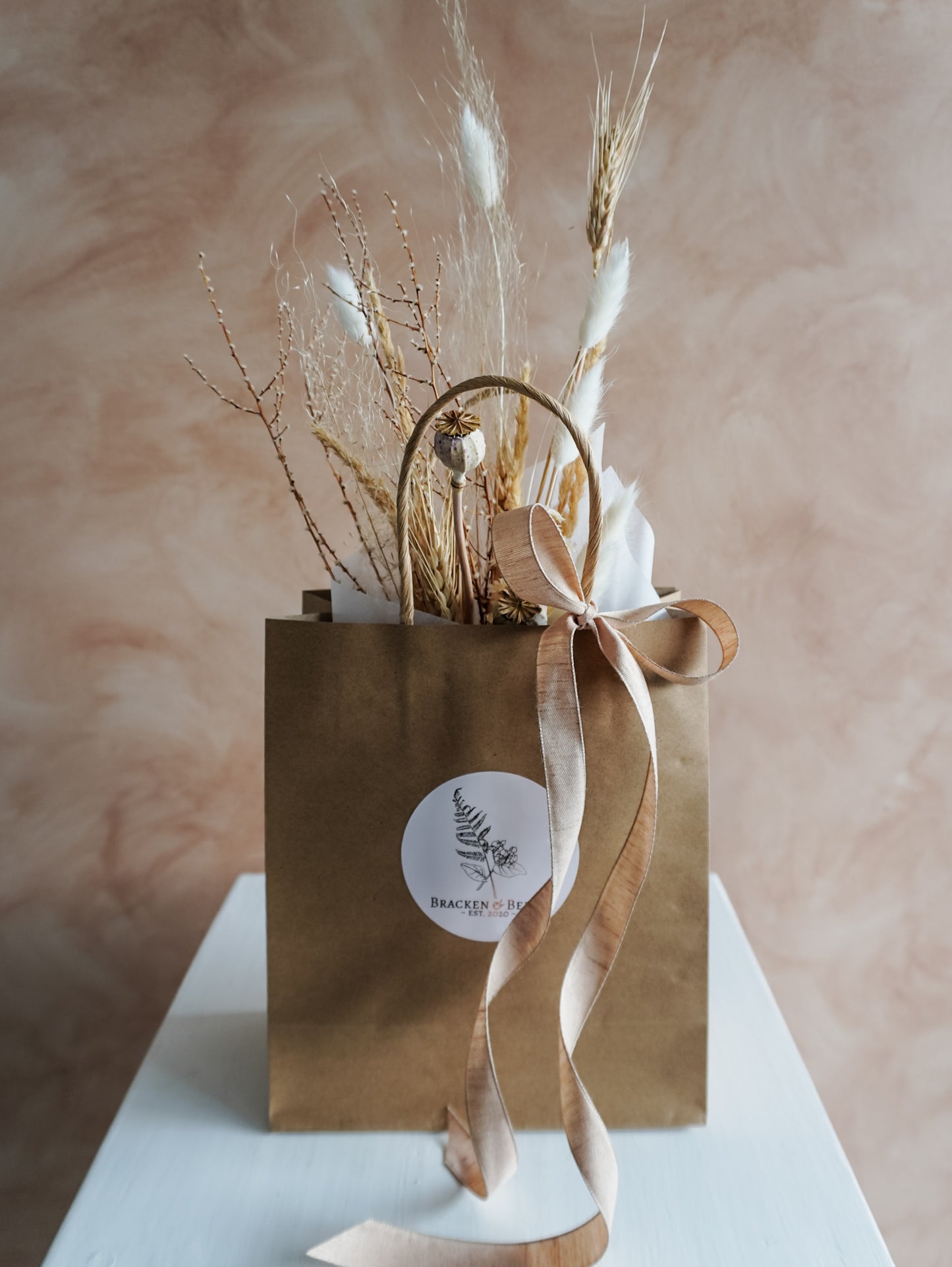 Brown paper bag with dried plants and a ribbon on a beige background