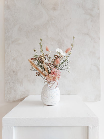 Dried flower arrangement in bud vase with pastel toned florals – distant view.