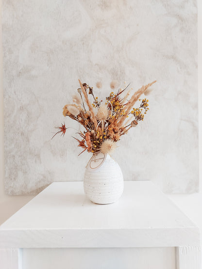 Dried flower arrangement in bud vase with orange florals – distant  full view.