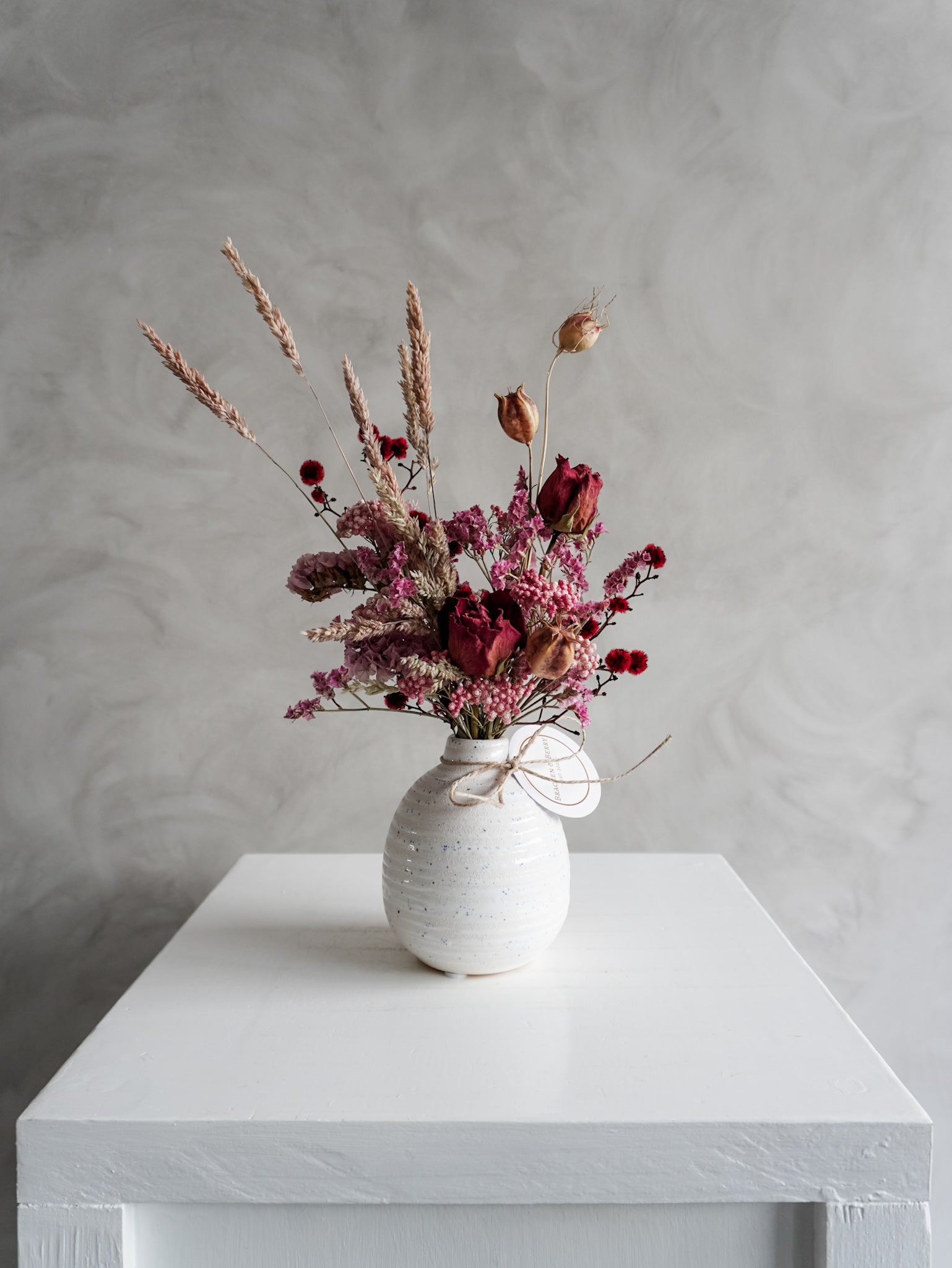 Dried flower arrangement in ceramic bud vase with pink and red  florals – distant view.