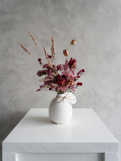 Dried flower arrangement in ceramic bud vase with pink and red  florals – distant view.