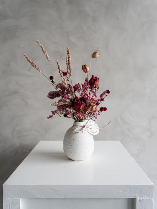 Dried flower arrangement in ceramic bud vase with pink and red  florals – distant view.