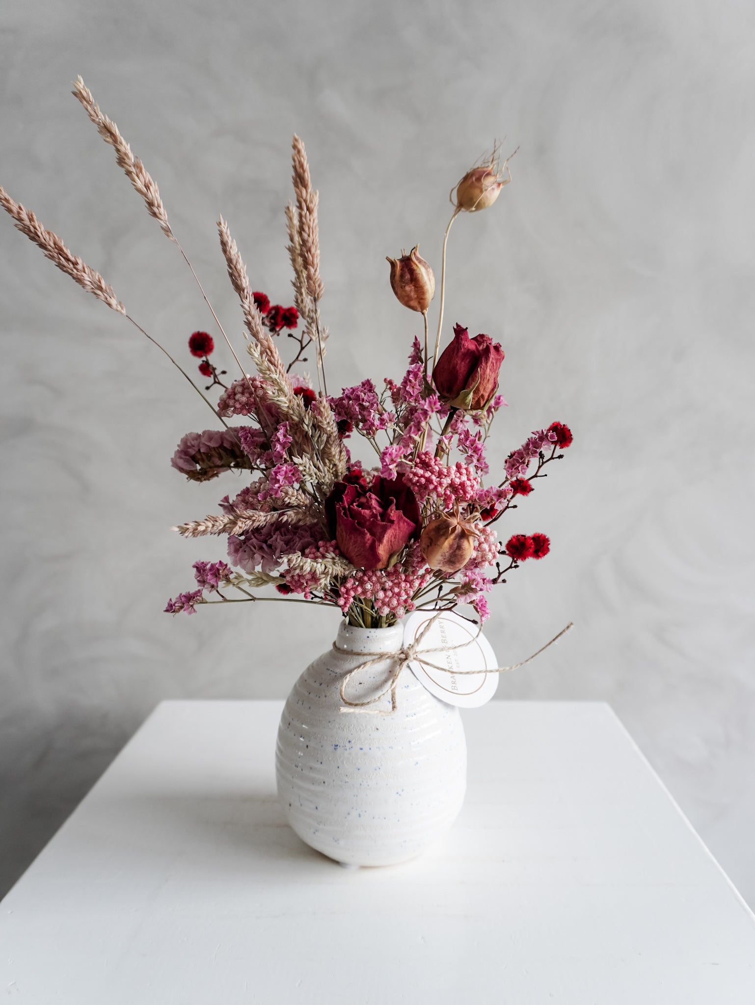 Dried flower arrangement in ceramic bud vase with pink and red  florals – close view.