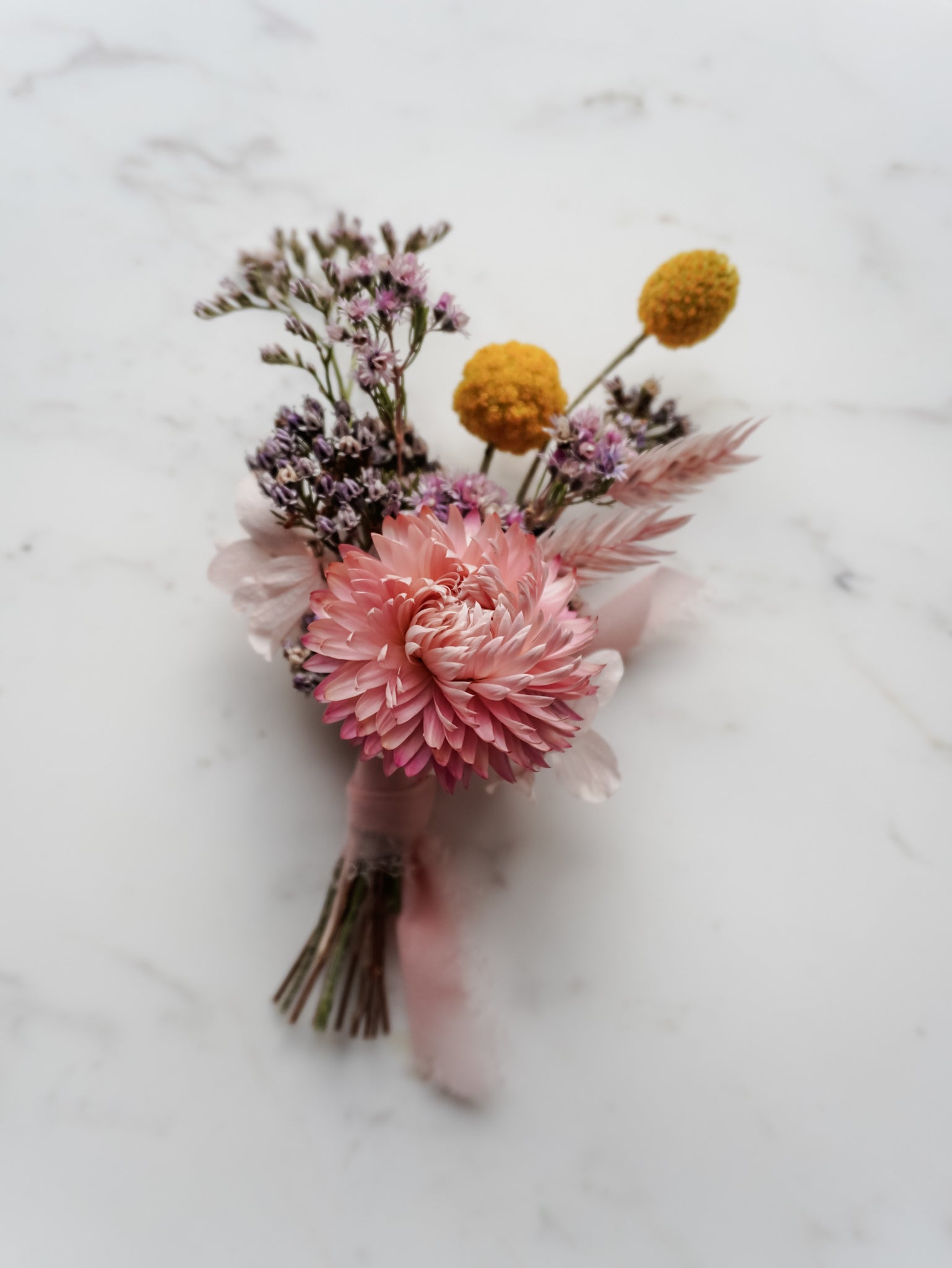 Buttonhole with dried pink and yellow flowers on a marble surface.