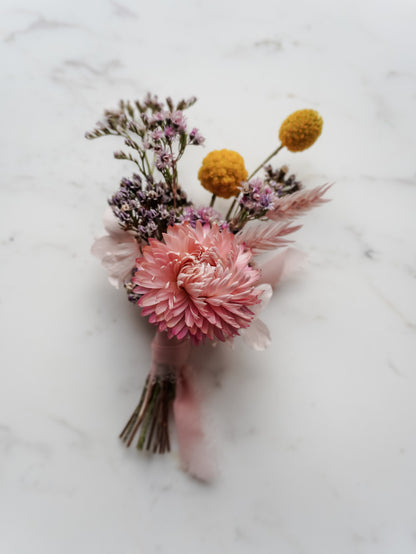 Buttonhole with dried pink and yellow flowers on a marble surface.