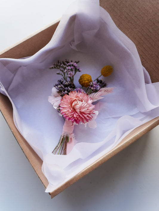 Buttonhole of dried flowers in a box with white tissue paper.