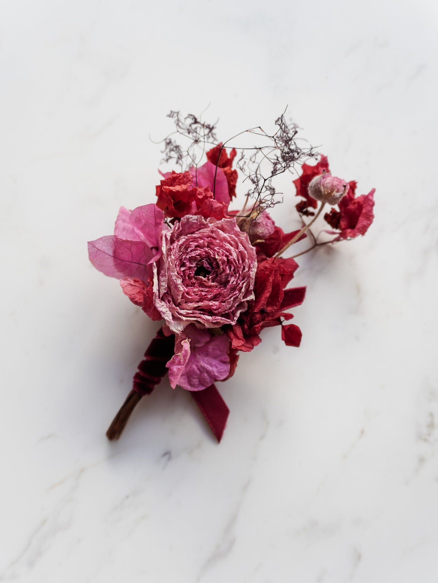 Dried pink floral boutonniere on a marble surface.
