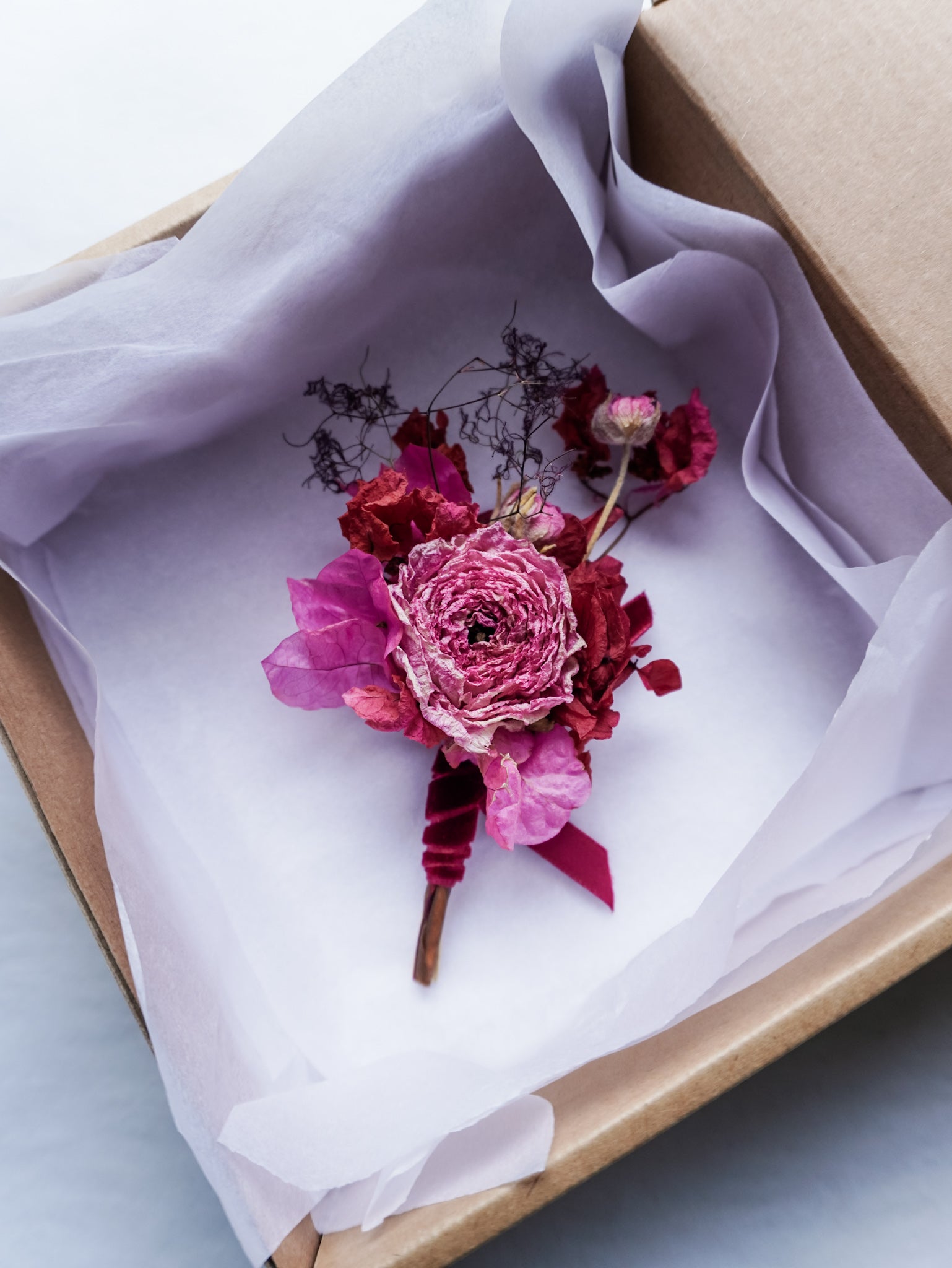 Dried pink floral boutonniere in a box with white tissue paper.