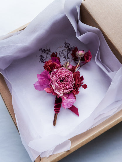 Dried pink floral boutonniere in a box with white tissue paper.