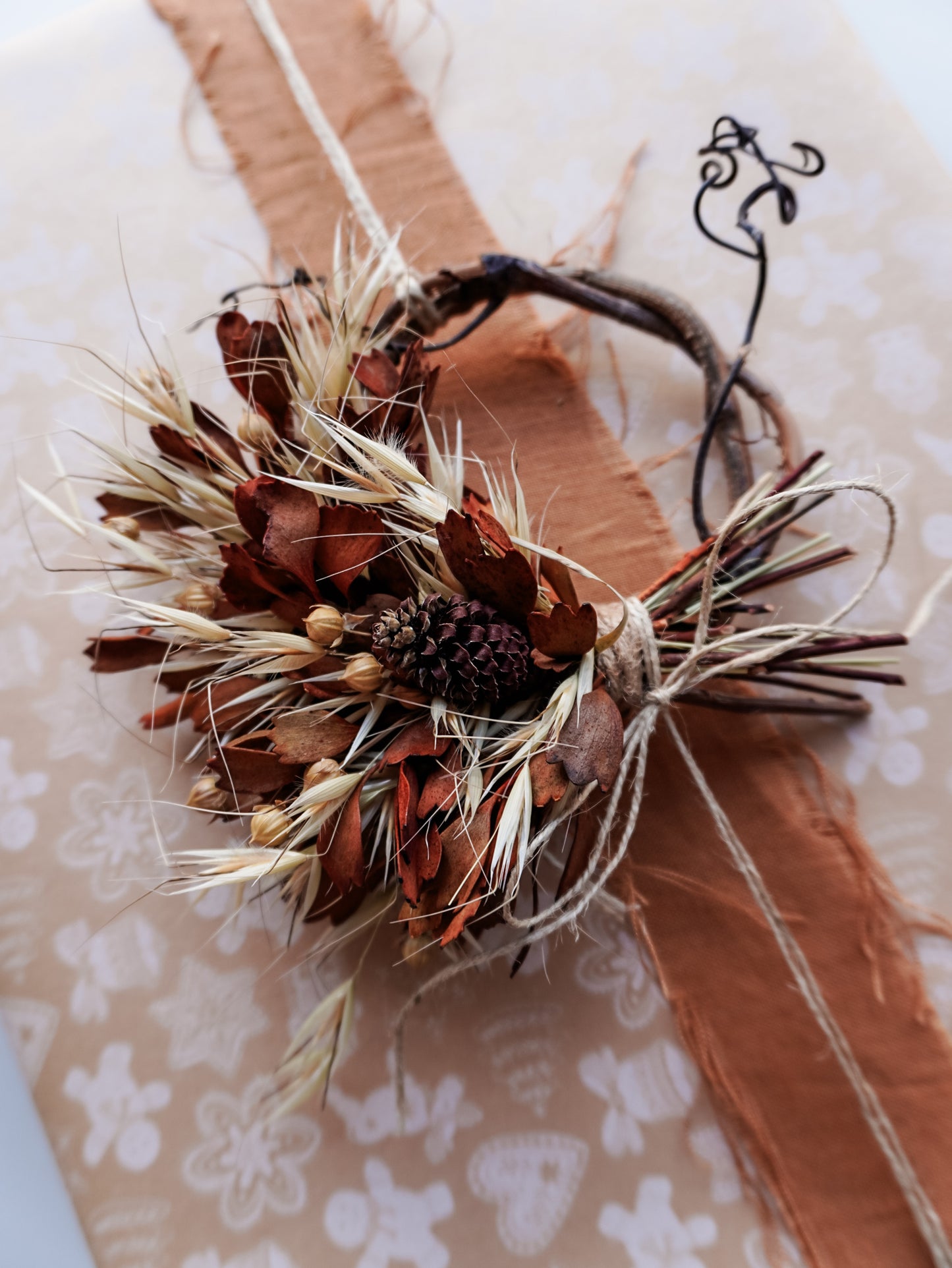 Dried flower mini wreath decoration in earthy tones on a grapevine base adorning a Christmas present.