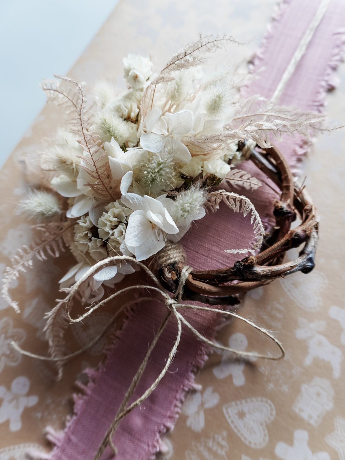 Dried flower mini wreath decoration in soft pink and white tones on a grapevine base adorning a Christmas present.