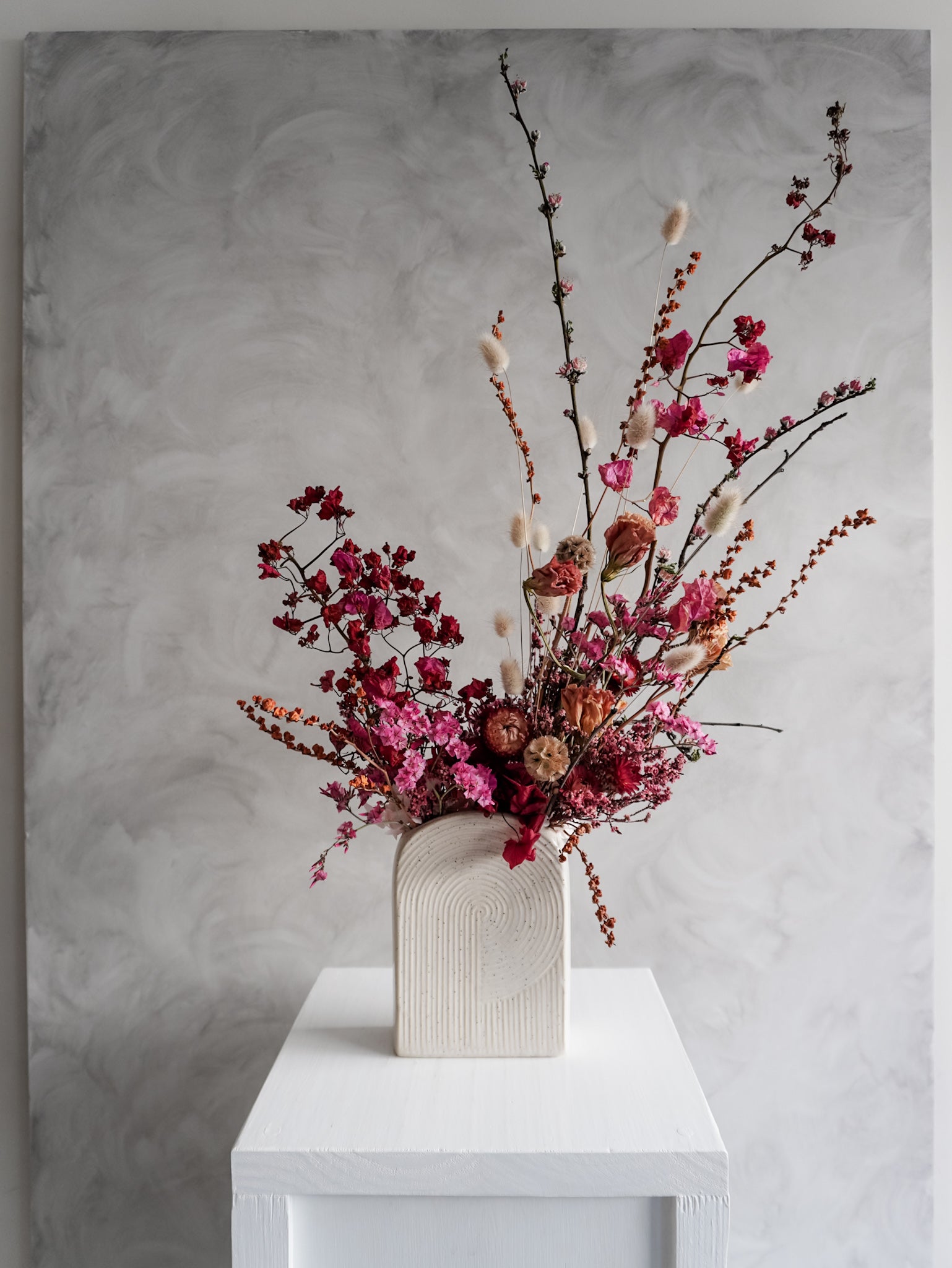 Dried flower arrangement in bold pink and red tones in a ceramic vessel – distant view.