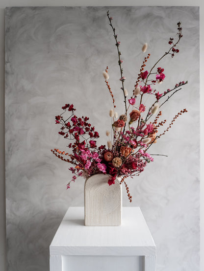 Dried flower arrangement in bold pink and red tones in a ceramic vessel – distant view.