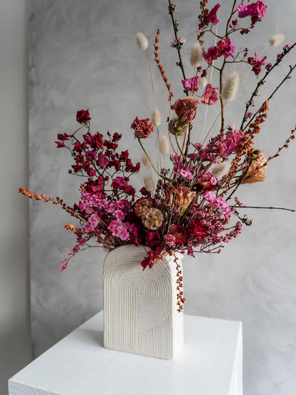 Dried flower arrangement in bold pink and red tones in a ceramic vessel – right side view.