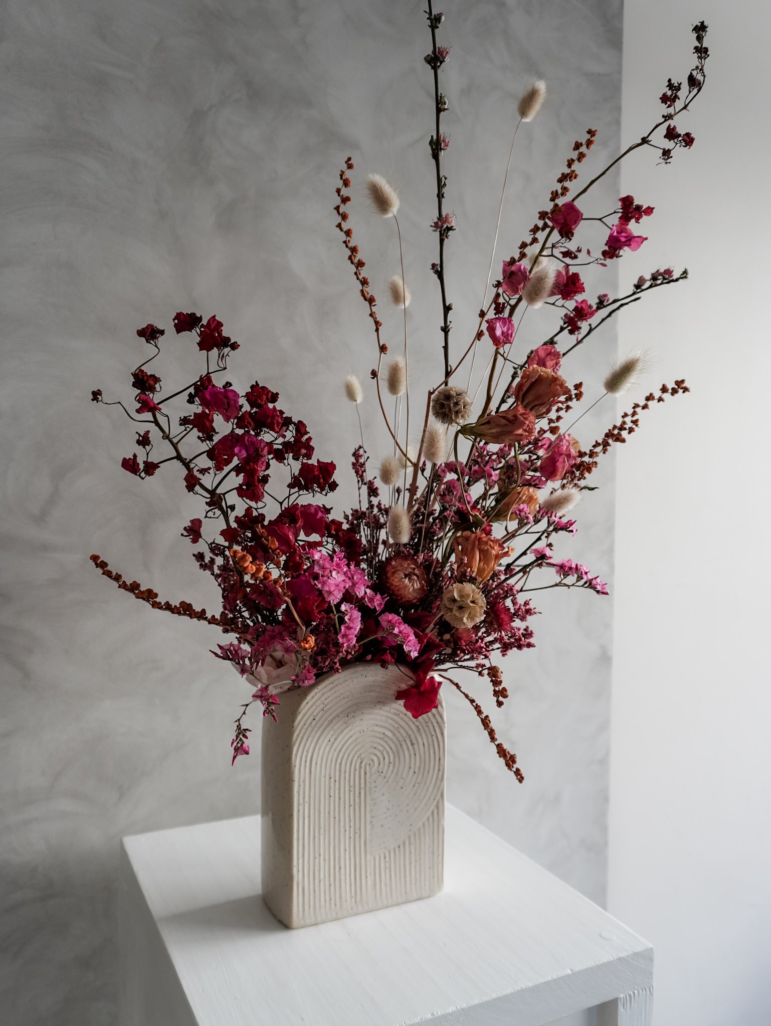 Dried flower arrangement in bold pink and red tones in a ceramic vessel – left side view.