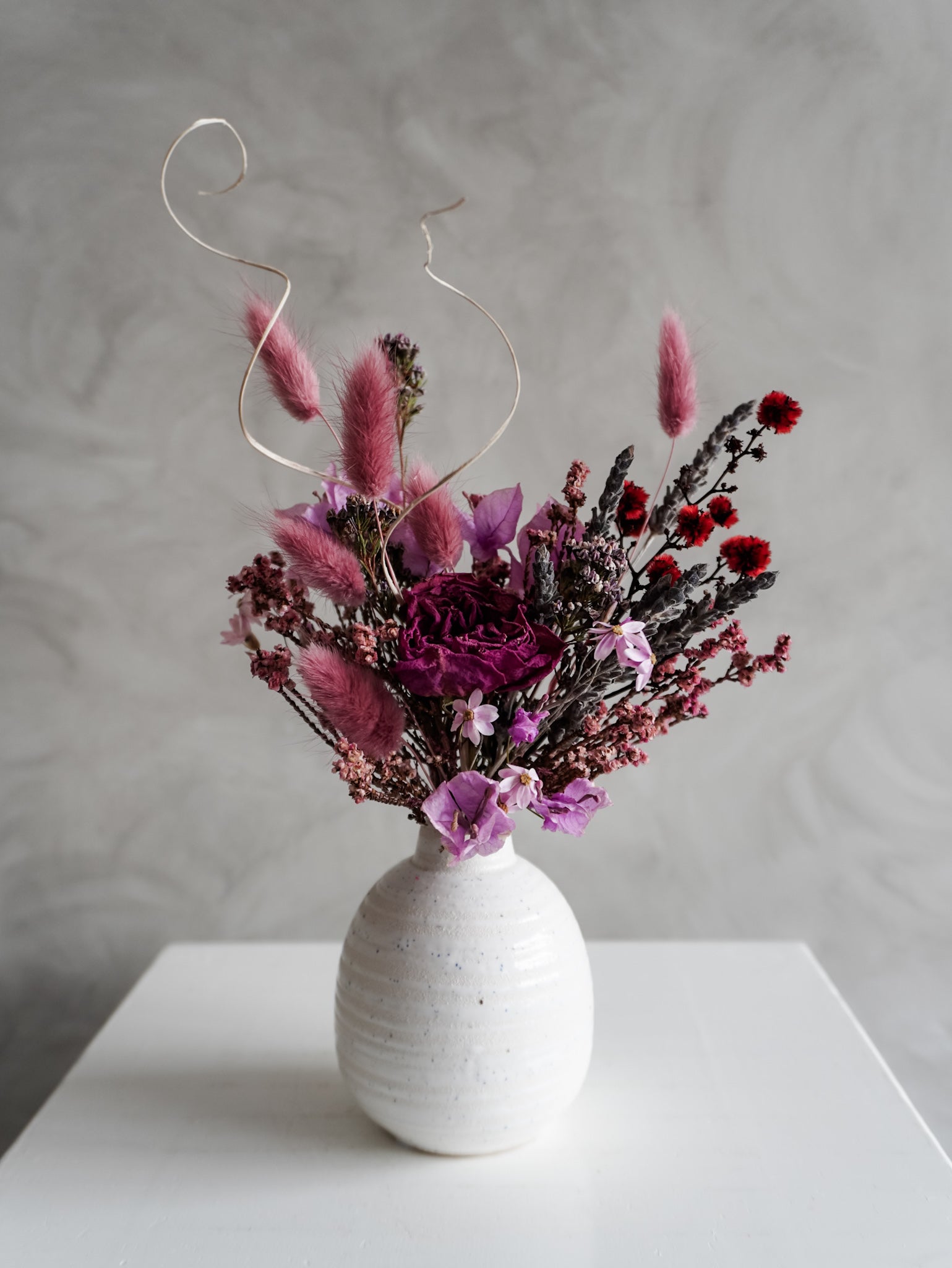 Dried flower arrangement in ceramic bud vase with deep violet and red florals – close view.