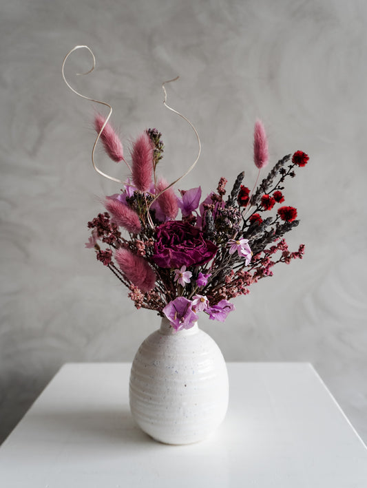 Dried flower arrangement in ceramic bud vase with deep violet and red florals – close view.
