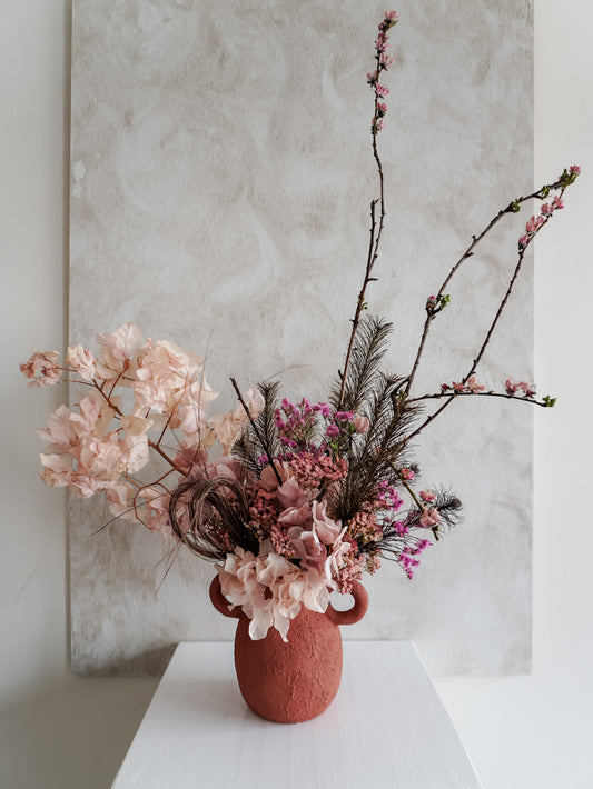 Dried flower arrangement in ceramic urn vase with rich berry tone florals – close view.