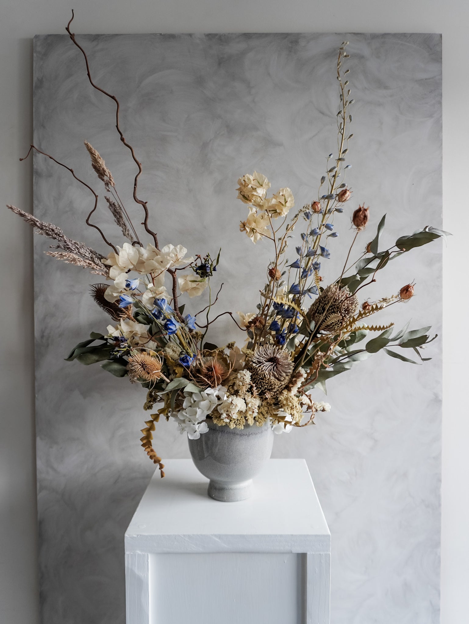 Neutral dried floral arrangement in a white vase against a gray textured wall.