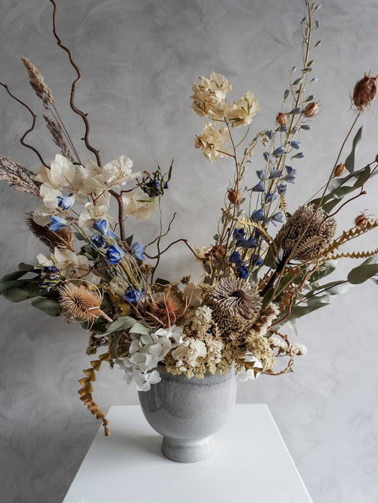 Neutral dried floral arrangement in a white vase against a gray textured wall.
