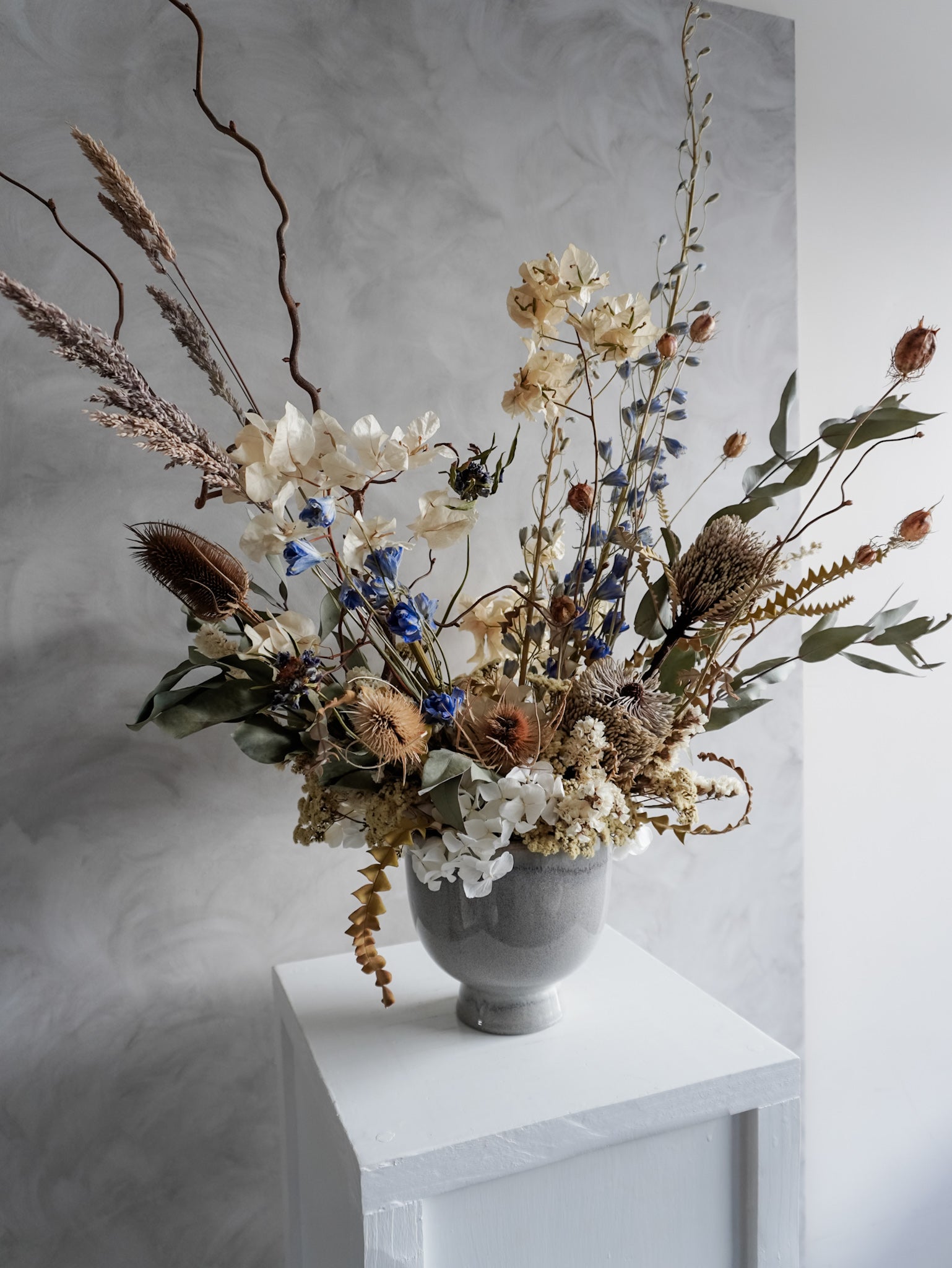 Neutral dried floral arrangement in a white vase against a gray textured wall.