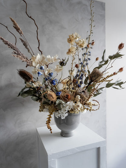Neutral dried floral arrangement in a white vase against a gray textured wall.